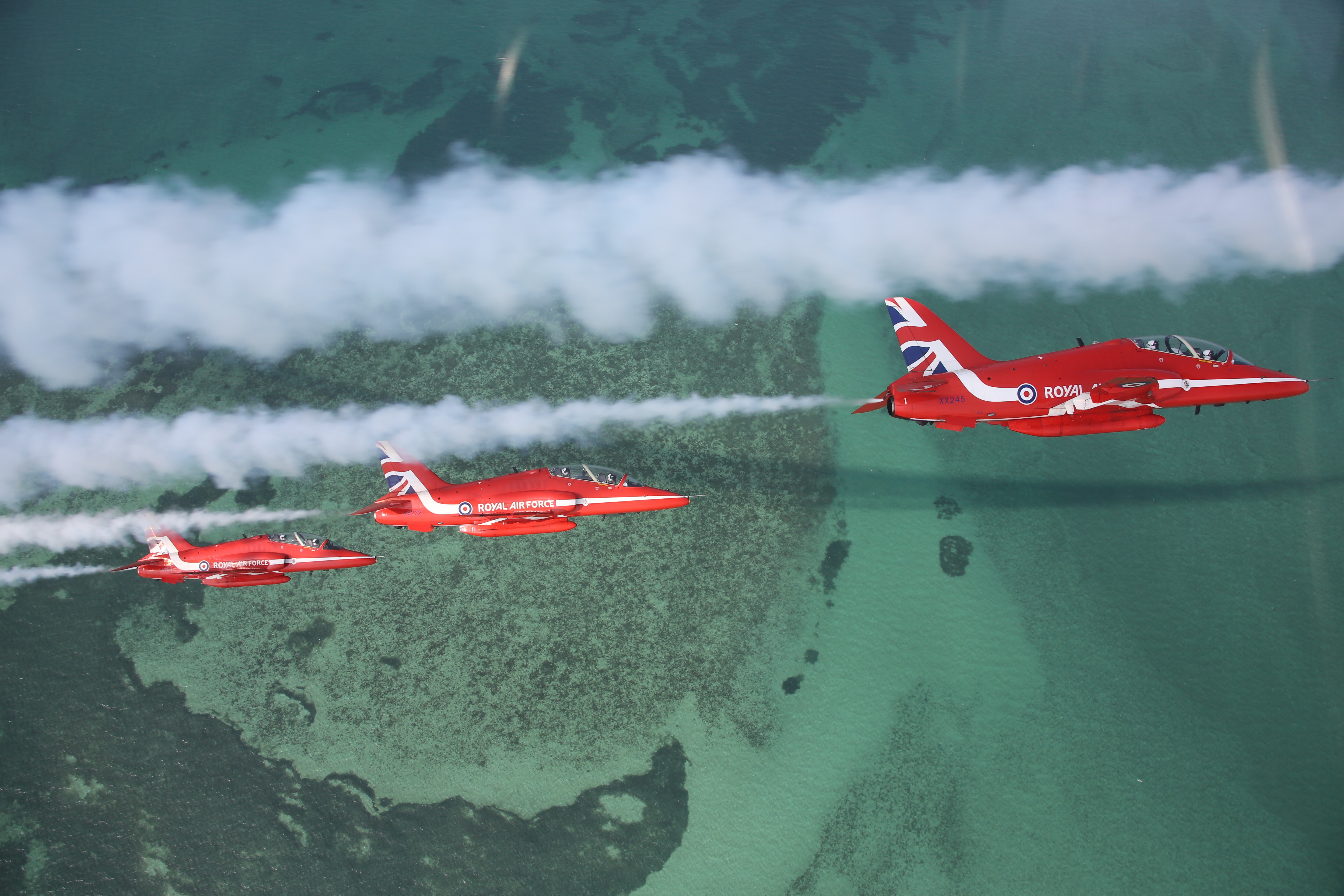 Image shows three Red Arrows performing with white smoke trails. 